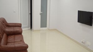 A room with a brown leather sofa, a flat-screen TV mounted on the wall, and a door leading to another room. - Descobrir Madeira com Carro Grátis (Estrada Padre Alfredo Vieira Freitas)
