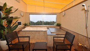 Un petit espace extérieur clos comprenant un jacuzzi, deux chaises en bois et une table.