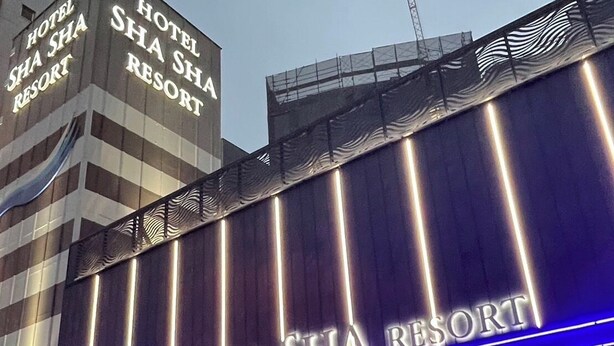 L’extérieur de l’hôtel Sha Sha Resort, avec une enseigne bien visible et un éclairage moderne.