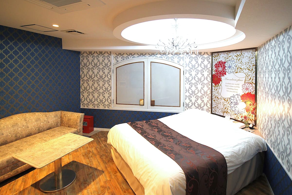 A hotel room with a bed, a sofa, a small table, a window, and a decorative wall panel.