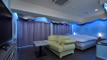 A modern hotel room with a flat-screen TV, a sofa, a bed, and a small table.