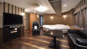Une chambre d’hôtel équipée d’un grand téléviseur à écran plat, d’un fauteuil massant, d’un lit, d’un canapé et d’une petite table.