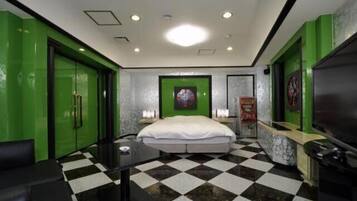 A hotel room with a checkered floor, green walls, a bed, a TV, and a desk with a chair.