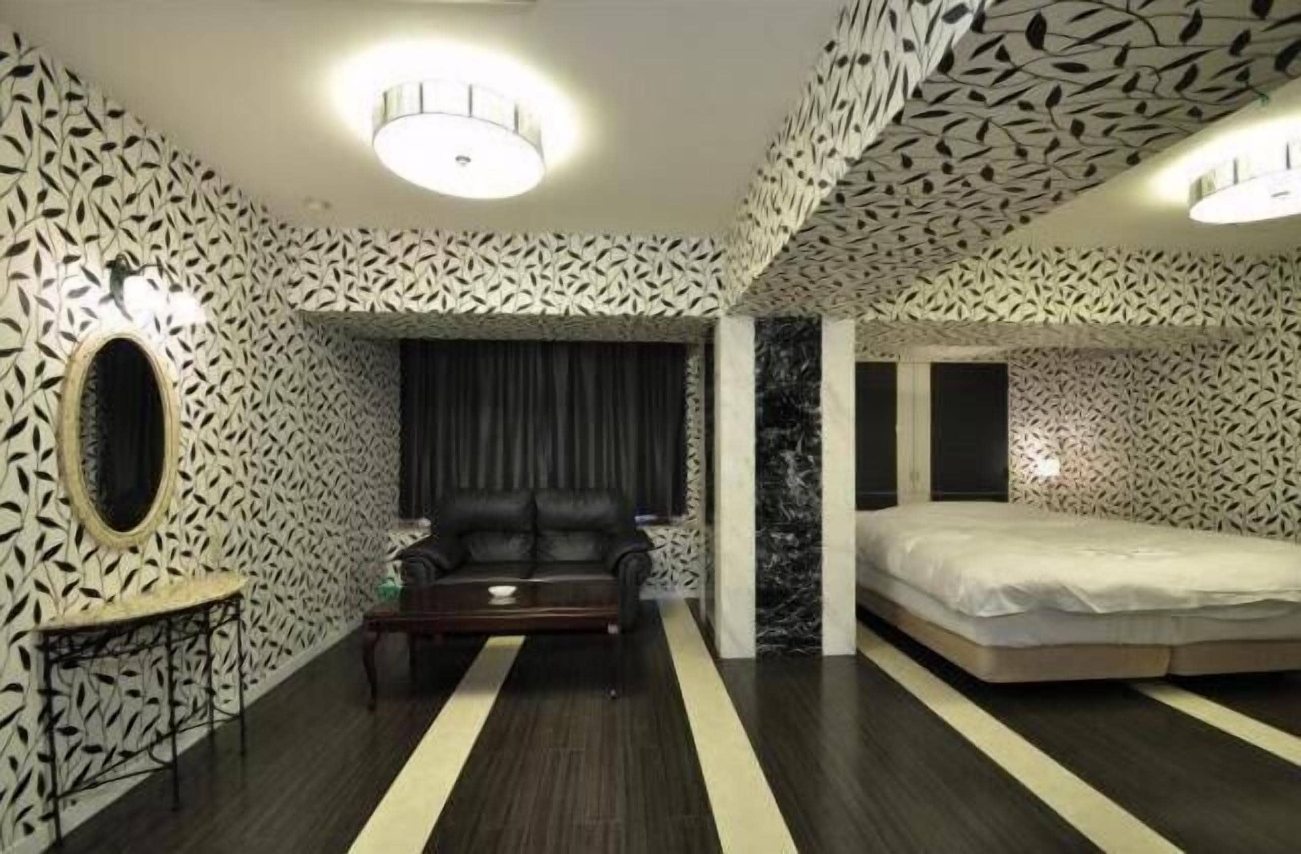 A modern bedroom with patterned walls, a black leather sofa, a bed, and a small table.