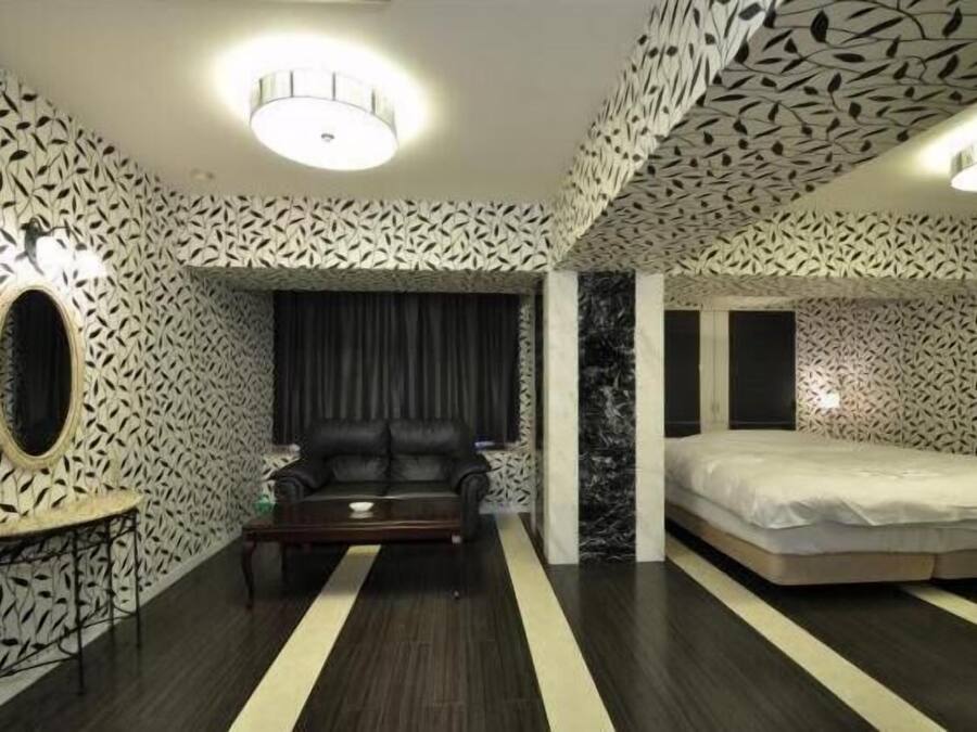 A modern bedroom with patterned walls, a black leather sofa, a bed, and a small table.