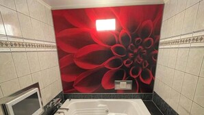 Un baño con una bañera grande, un tocador con espejo y un diseño floral rojo en la pared.