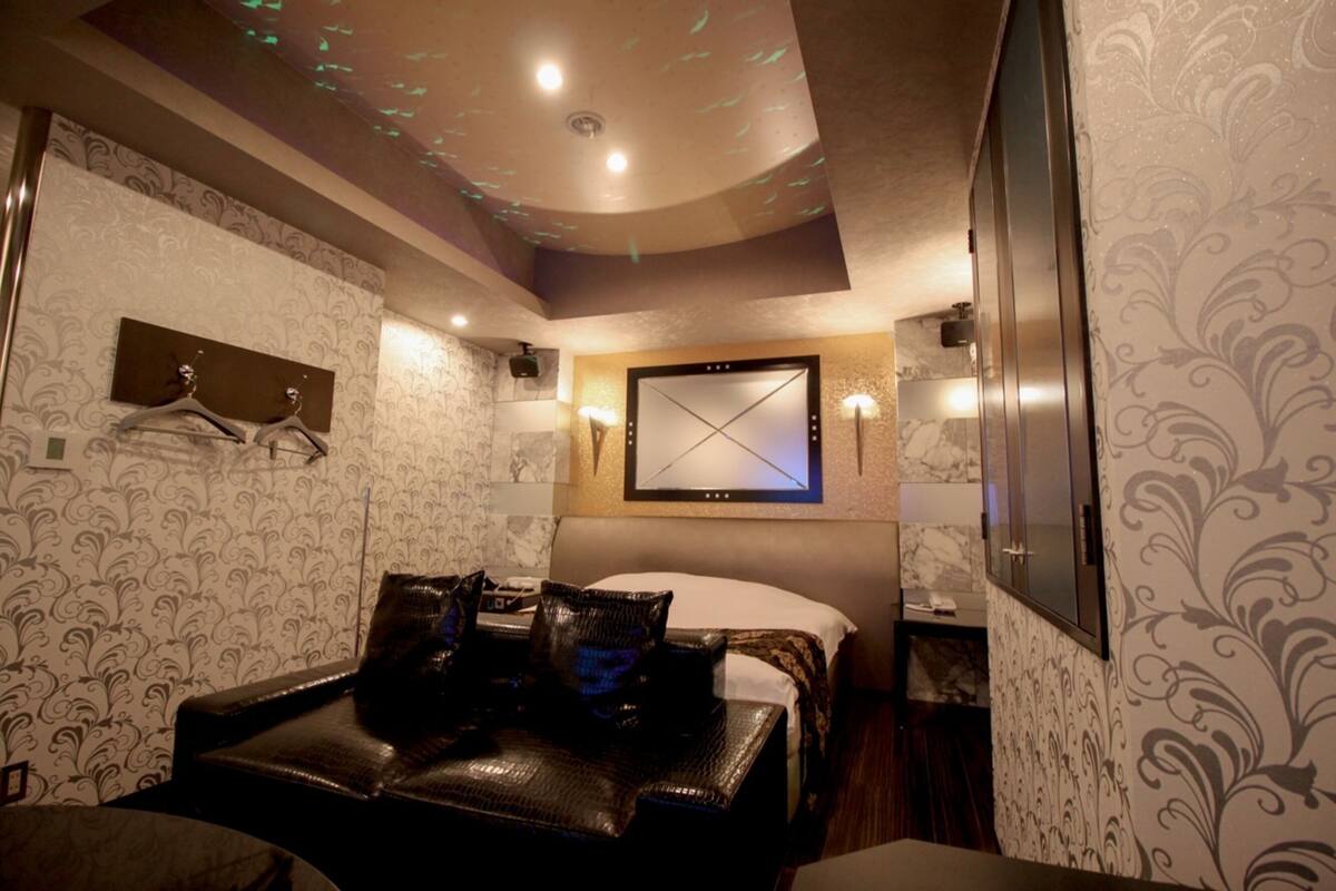 A hotel room with a bed, a seating area with a leather sofa, a wall-mounted TV, and a ceiling with a light fixture.