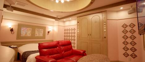 Una habitación de hotel con un sofá de cuero rojo, una mesa redonda, una cama con cubrecama blanco y un armario de madera.