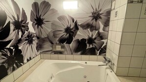 Un baño con una bañera grande, paredes de azulejos y un mural floral.