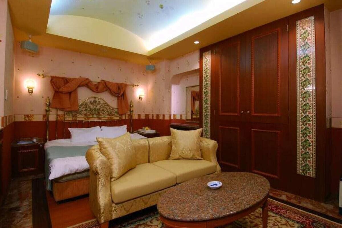A hotel room with a bed, sofa, round table, and wardrobe.