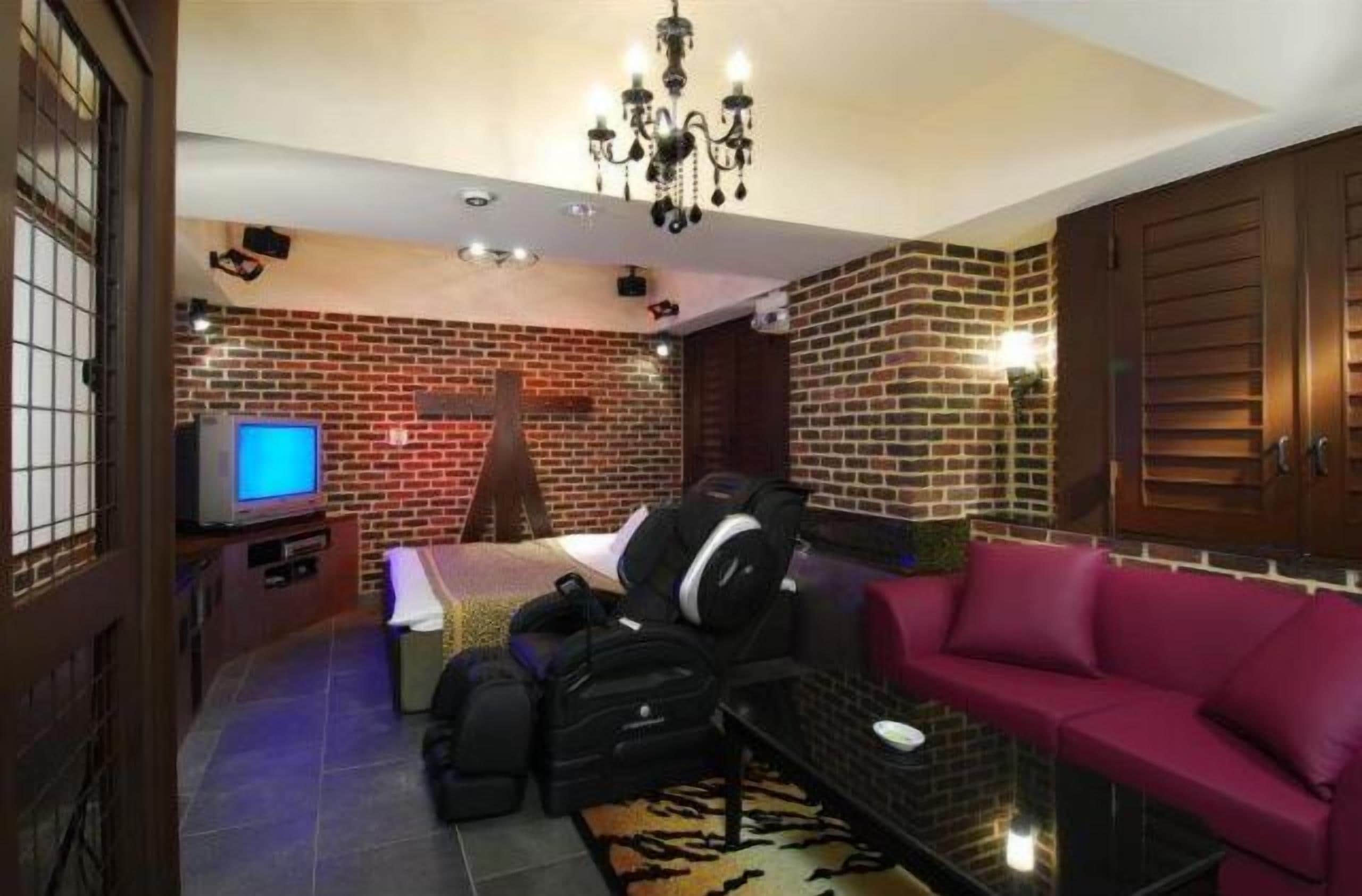 Een kamer met een bakstenen muur, een bed, een televisie, een bank en een kroonluchter.
