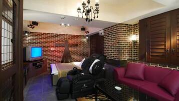 Una habitación con pared de ladrillo, cama, televisor, sofá y candelabro.