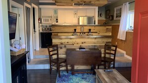Una cocina moderna con detalles de madera, un comedor con mesa y sillas, y una puerta roja.