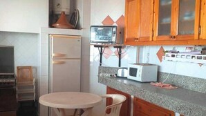 Una cocina compacta con un refrigerador blanco, un microondas y una tostadora sobre la encimera. Hay una pequeña mesa redonda con dos sillas.