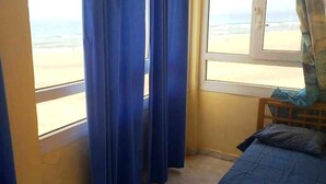 Una habitación con una cama, una ventana con cortinas y vista a la playa.