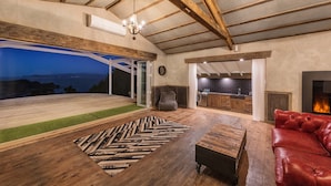 A spacious living area with a wooden ceiling, a large window overlooking a scenic view, a red leather sofa, and a fireplace.