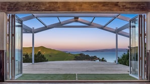 An open patio with a glass enclosure, a wooden deck, and a view of a hilly landscape and water body.