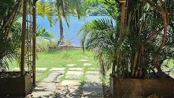 A covered outdoor area with a view of a body of water, surrounded by lush greenery and a stone pathway.