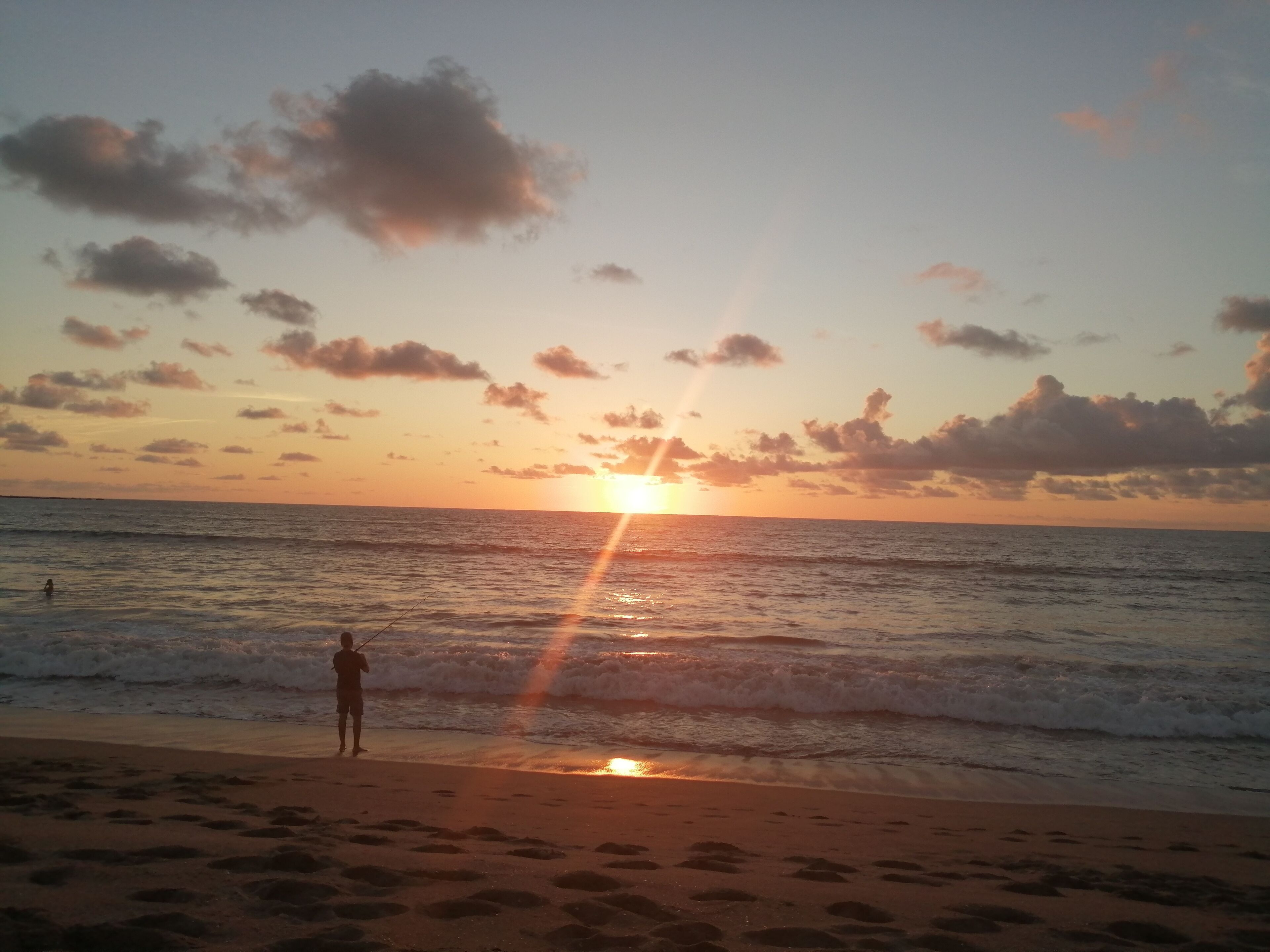 A beach scene with a person standing near the water during sunset.