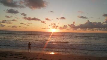 A beach scene with a person standing near the water during sunset.