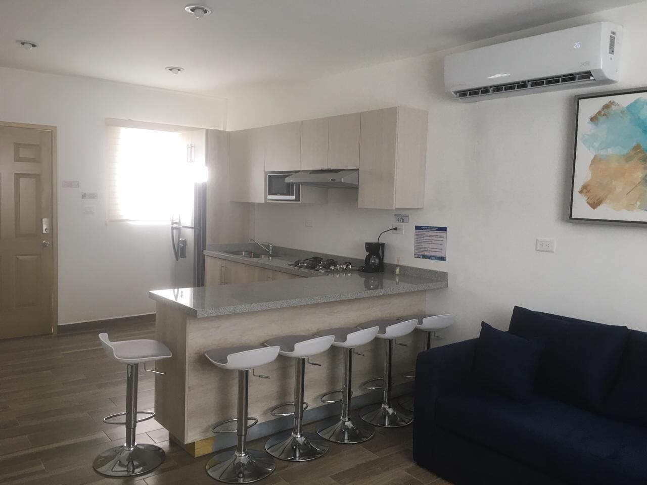Een moderne keuken met een centraal eiland, barkrukken, een donkerblauwe bank en een airconditioning.