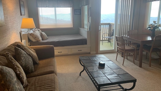 A cozy living room with a sofa, a coffee table, a window seat, and a dining area with chairs and a table. - 10-202 (Banner Elk)