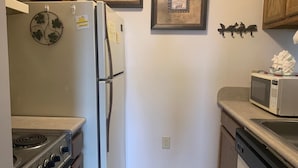 A kitchen with a refrigerator, stove, microwave, and dishwasher. There are wooden cabinets and a wall-mounted clock. - 10-202 (Banner Elk)