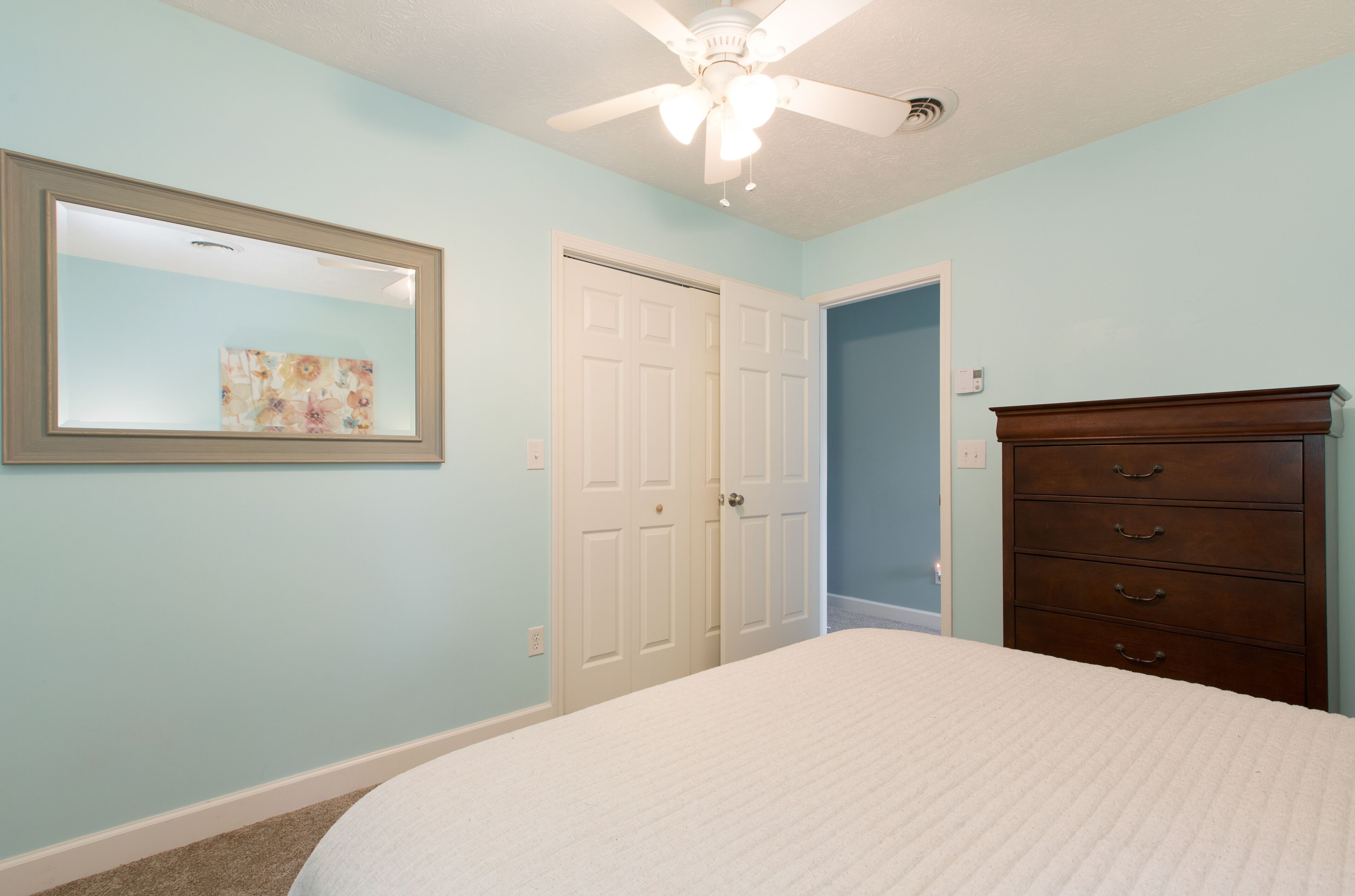 Un dormitorio con cama, cómoda, ventilador de techo y puerta.