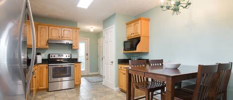 A kitchen with wooden cabinets, a stainless steel refrigerator, a microwave, an oven, and a dining table with chairs.
