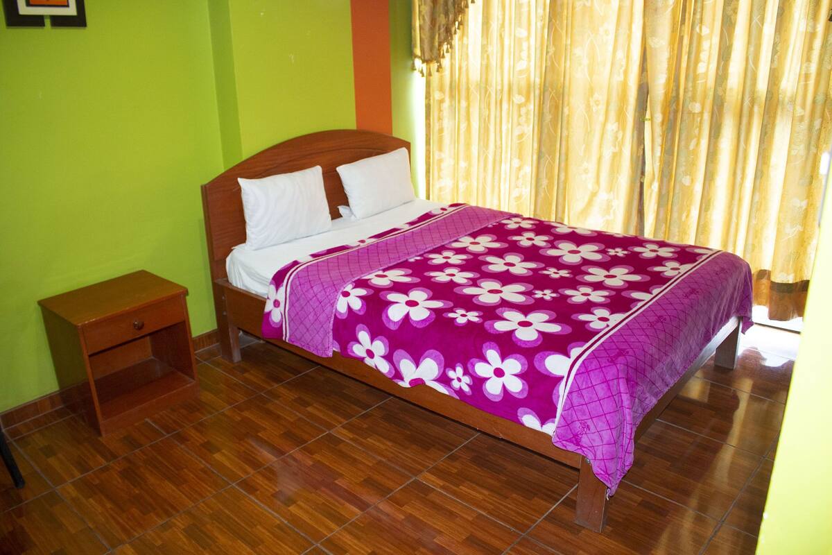 A bed with a floral bedspread, a wooden headboard, and a nightstand.