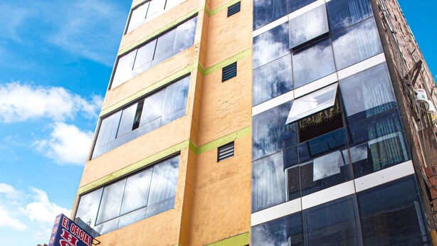 A multi-story building with a mix of brick and glass facades, a visible storefront with a sign, and a clear blue sky in the background. - Hospedaje el Oficial (Cusco)