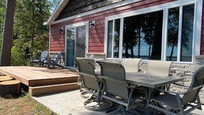 An outdoor patio with a wooden table and chairs, a stone bench, and a view of a lake. - Calling Outdoor Adventurers! Resting on Grace Lake House with Home Theater! (Bemidji)