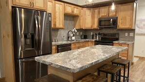 A modern kitchen with wooden cabinets, stainless steel appliances, granite countertops, and bar stools. - Calling Outdoor Adventurers! Resting on Grace Lake House with Home Theater! (Bemidji)