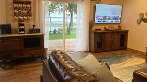 A living room with a leather couch, a coffee station, a flat-screen TV, and a view of the outdoors. - Calling Outdoor Adventurers! Resting on Grace Lake House with Home Theater! (Bemidji)