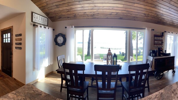 A dining area with a round table and chairs, a clock, and a view of the outdoors. - Calling Outdoor Adventurers! Resting on Grace Lake House with Home Theater! (Bemidji)