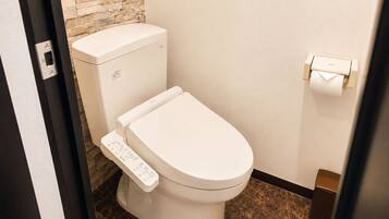 A modern toilet with a control panel, a toilet paper holder, and a stone wall in the background.