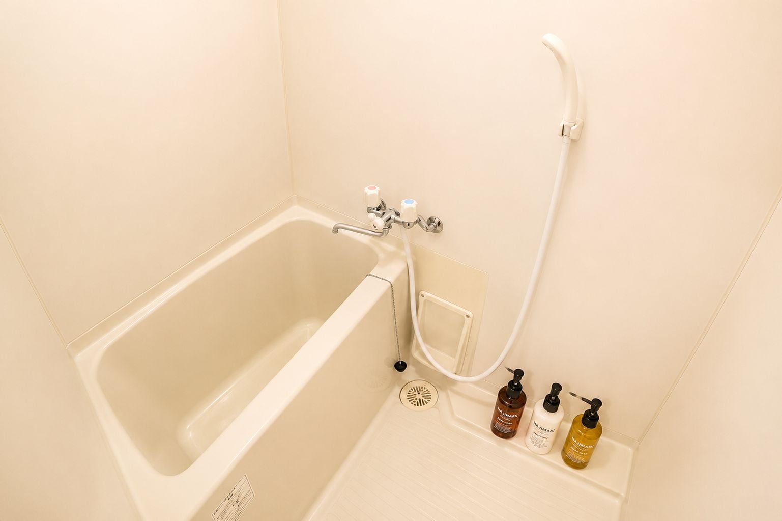 A bathroom with a bathtub, a shower, and three bottles of toiletries.