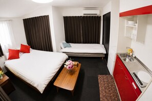 A hotel room with two beds, a wooden nightstand, a small table with a vase of flowers, a red cabinet with a sink, and a mirror above the cabinet. - Royal Heights Sakuragawa Condominium (Osaka)