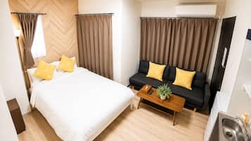 A hotel room with a bed, a sofa, a coffee table, and an air conditioning unit.