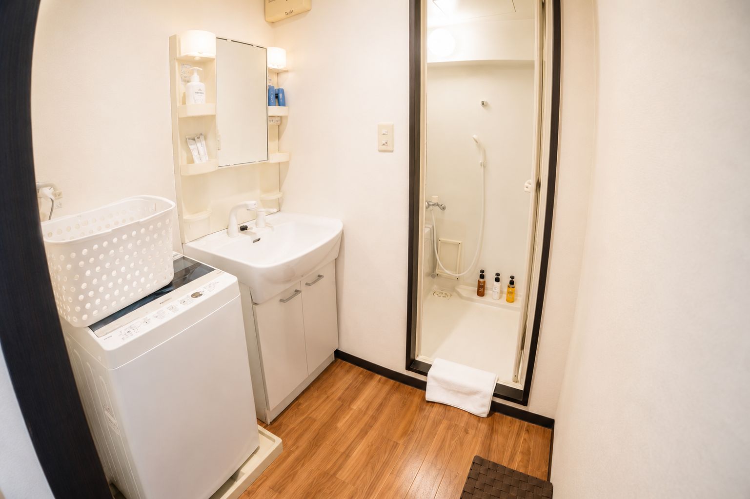 Een compacte badkamer met een wasmachine, een wastafel en een douchecabine.