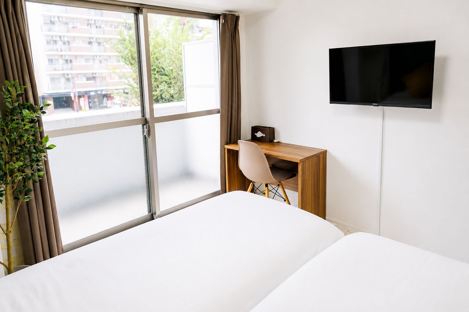 A hotel room with a bed, a desk, a chair, a TV, and a window with curtains.