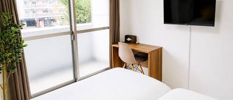 A hotel room with a bed, a desk, a chair, a TV, and a window with curtains.