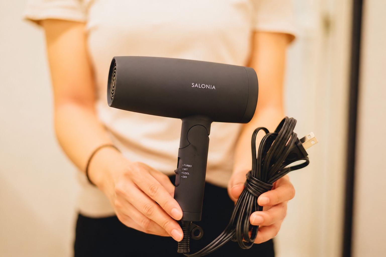 A person holding a black hairdryer with a cord, labeled 'SALONIA.'