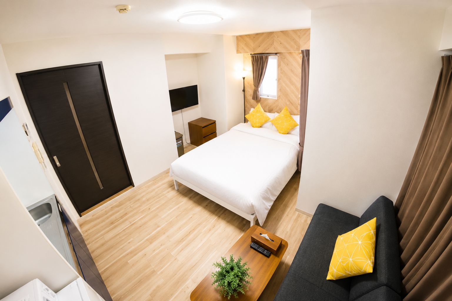 Een hotelkamer met een bed, een bank, een televisie, een bureau en een raam met gordijnen.