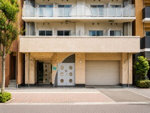 A multi-story building with a flat roof, a central entrance with a large door, and a covered parking area. - Royal Heights Sakuragawa Condominium (Osaka)