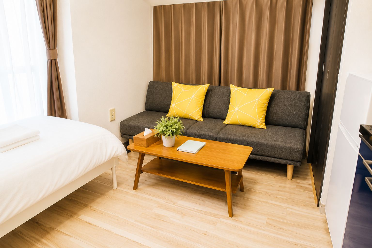 Ein Hotelzimmer mit einem Bett, einem Sofa mit gelben Kissen, einem Holztisch mit einer Pflanze und einem Vorhang.