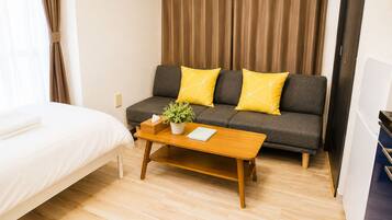 Ein Hotelzimmer mit einem Bett, einem Sofa mit gelben Kissen, einem Holztisch mit einer Pflanze und einem Vorhang.