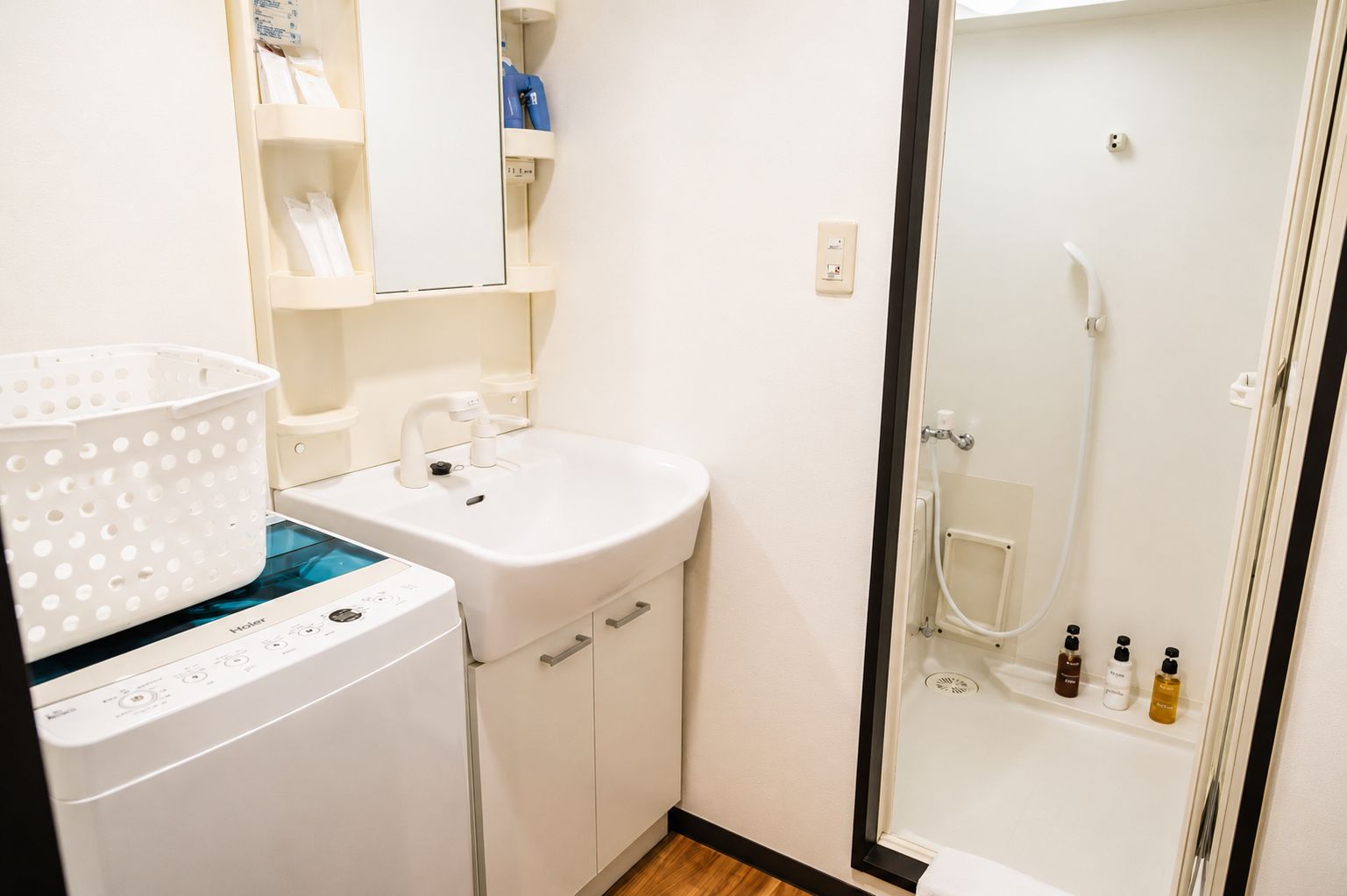 A compact bathroom with a washing machine, a sink, and a shower area.