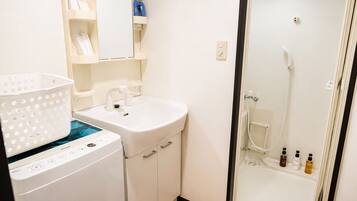 A compact bathroom with a washing machine, a sink, and a shower area.