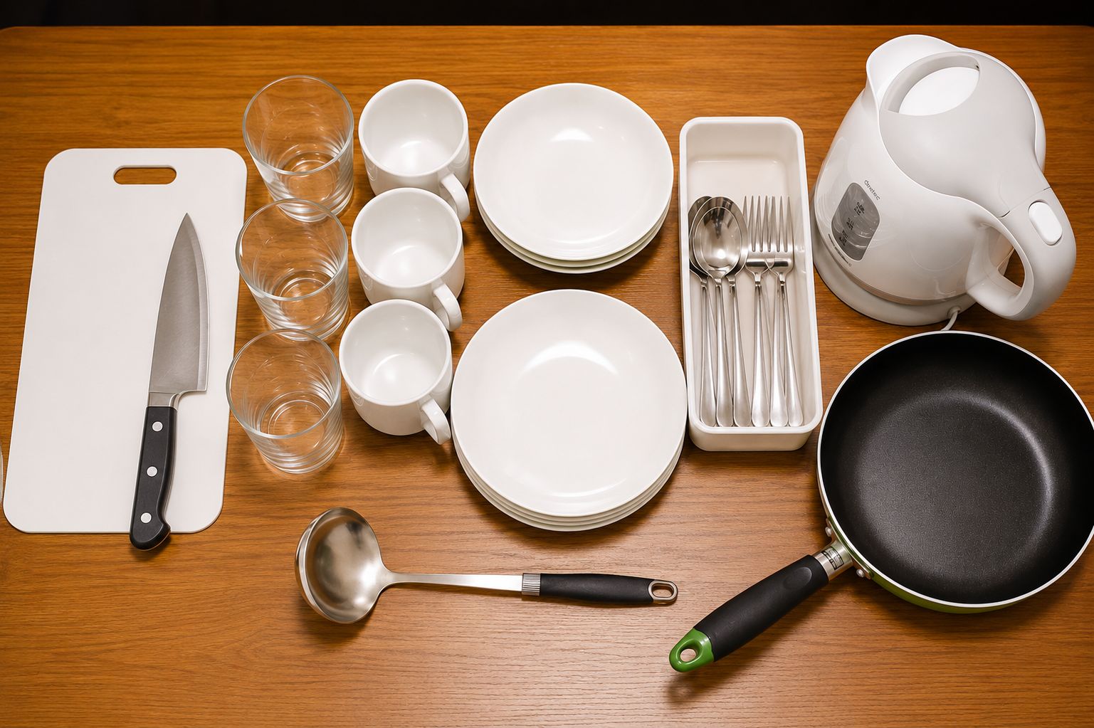 A wooden table with a white cutting board, a knife, several white cups, a stack of white plates, a white kettle, a set of silverware, a black frying pan, and a metal ladle.